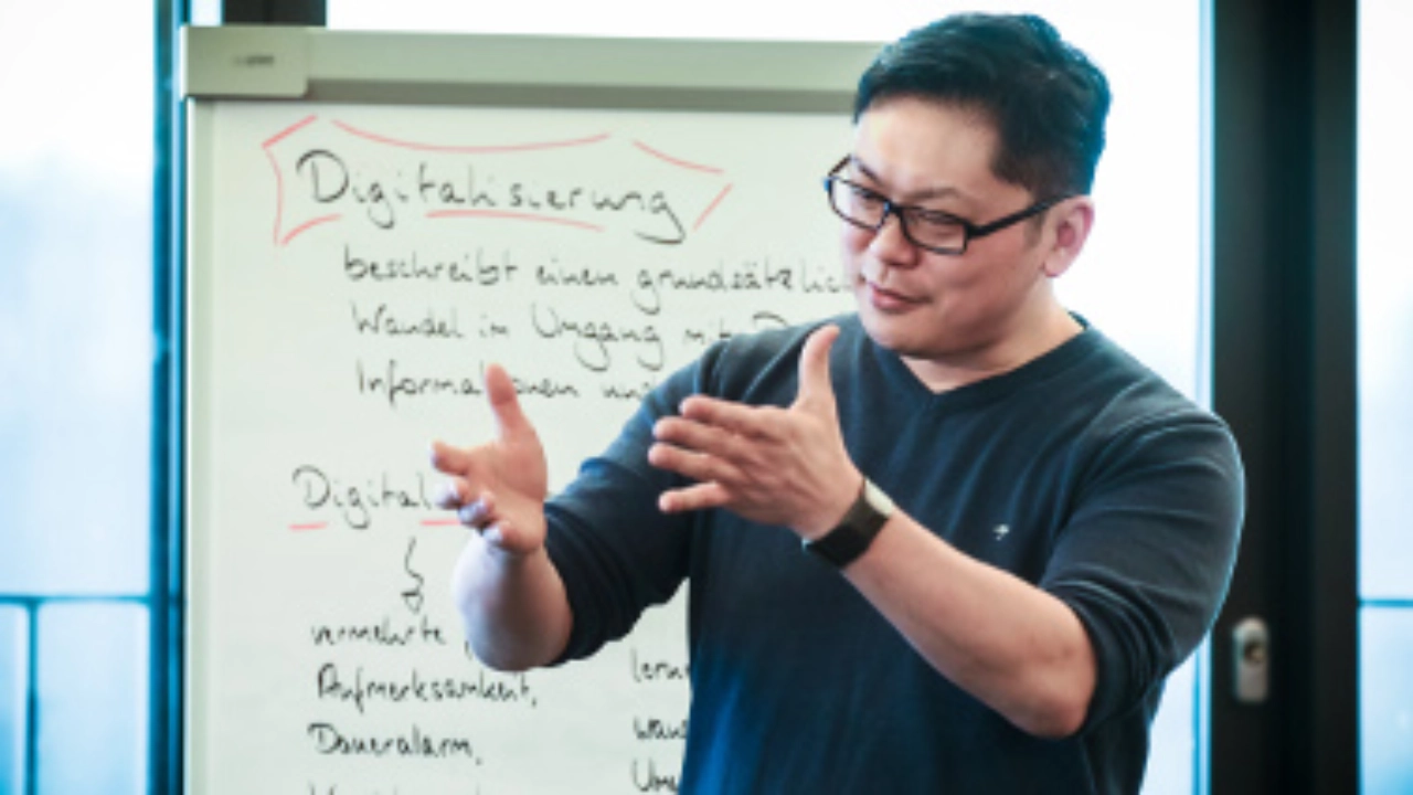 Ein junger Mann steht gestikulierend vor einer Metaplanwand.