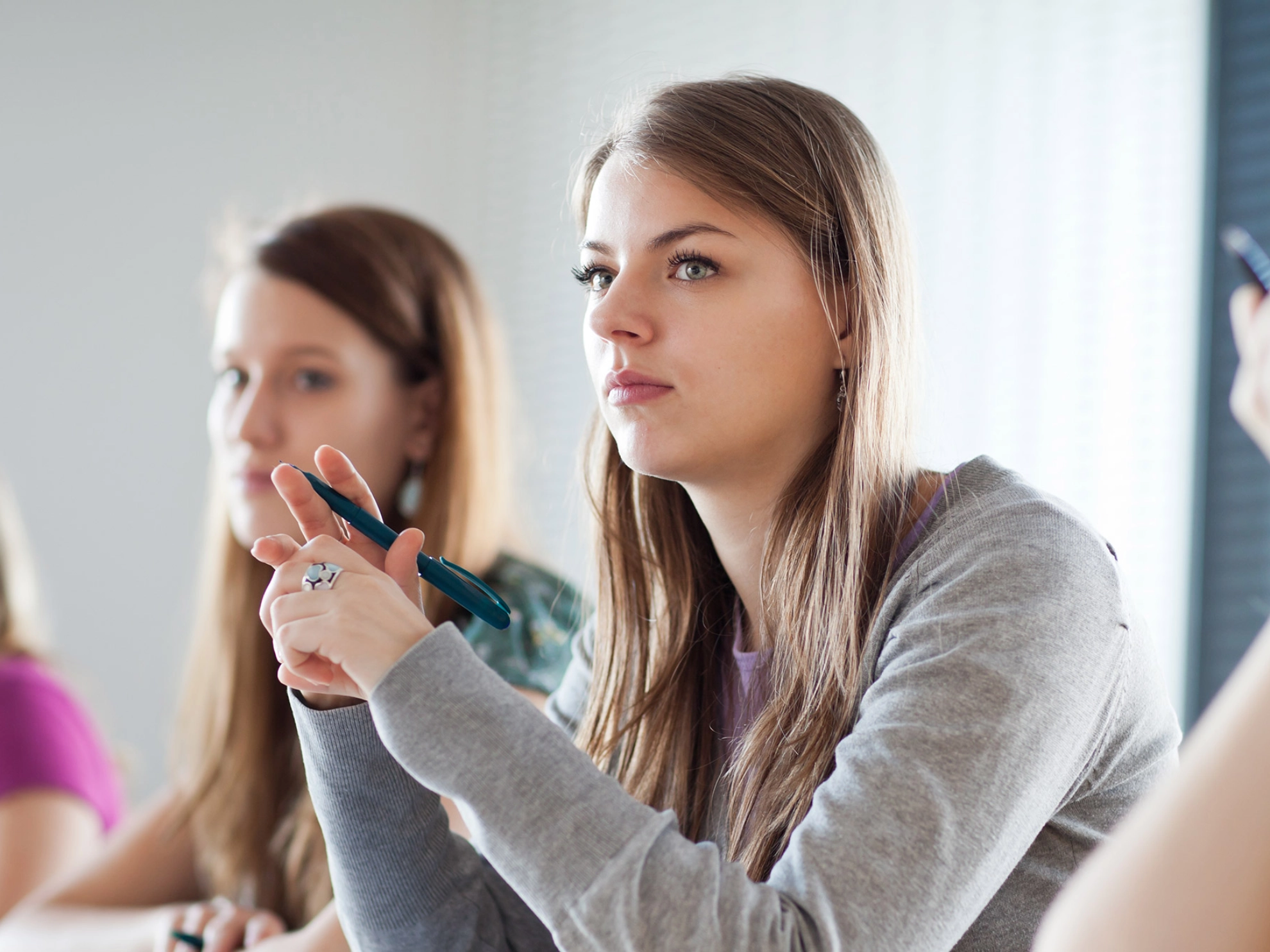 Eine Studentin sitzt zwischen ihren Kommolitonen während eines Seminars und macht Notizen.