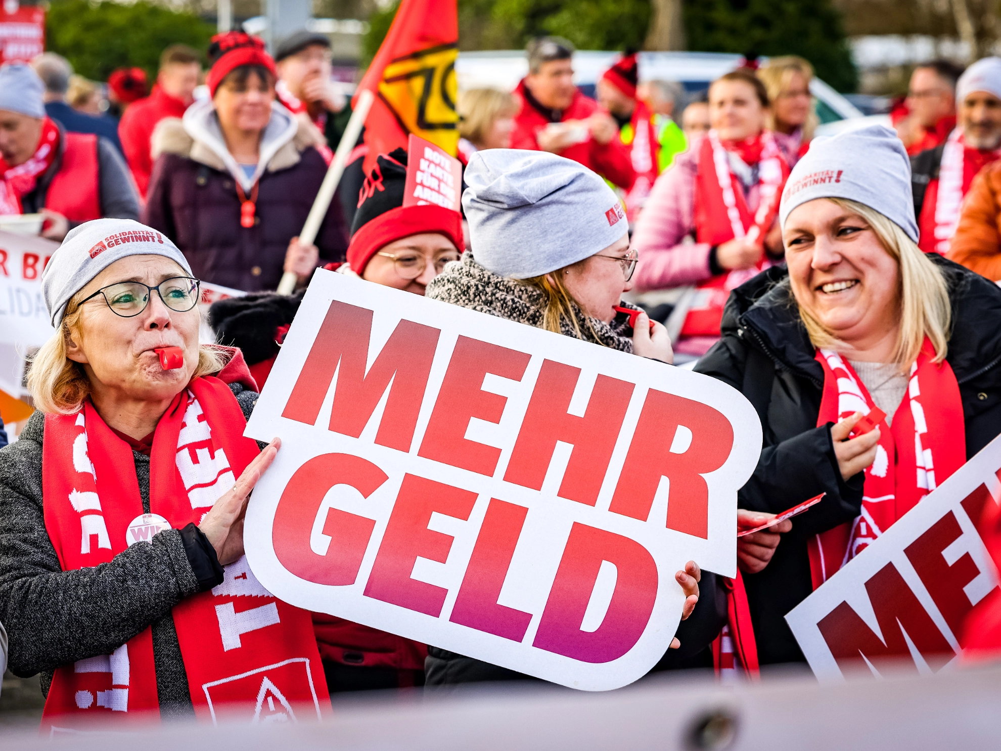 Drei Frauen auf der Demonstration in Kaarst. Eine Frau hält ein Schild „Mehr Geld“ hoch.