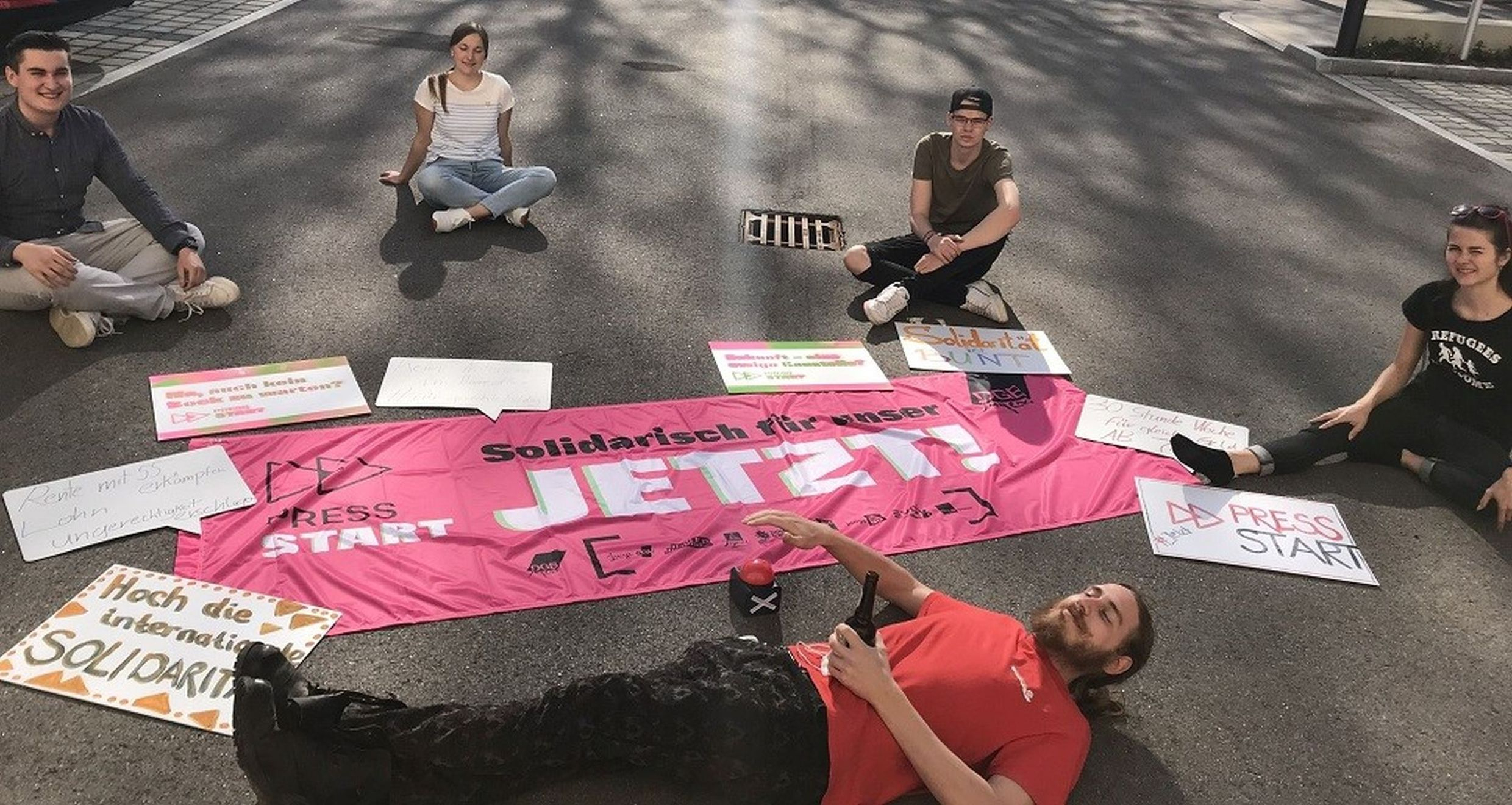 5 studierende sitzen im Kreis um Plakate zum Aufruf von Solidarität.