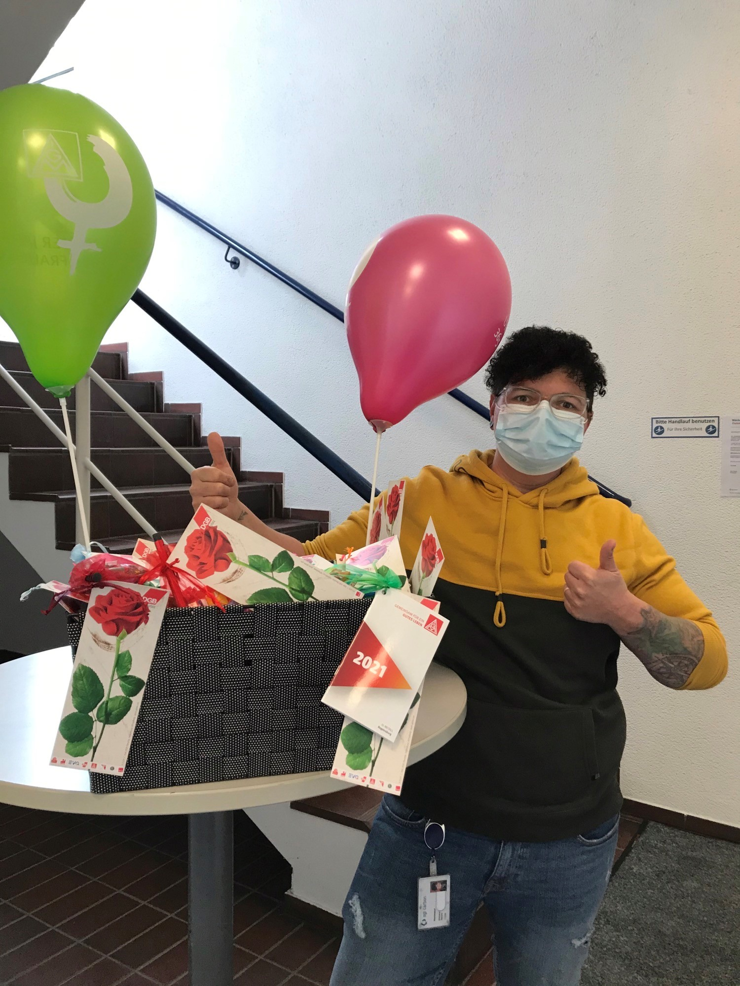 Eine Frau zeigt den Daumen hoch und steht hinter einer Kiste mit Präsenten zum Frauentag.